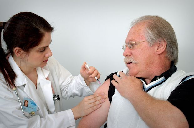 Middle aged man receiving an intramuscular immunization into his left shoulder muscle from a female nurse